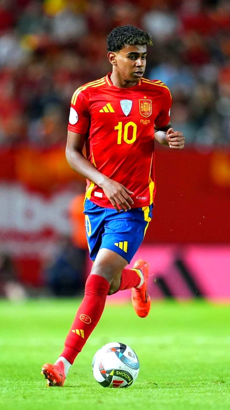 A male soccer player wearing a red and yellow Spain jersey with number 10 controls the ball on the field during a match, as a crowd and stadium blur in the background—a scene often enjoyed by fans via IPTV French broadcasts.