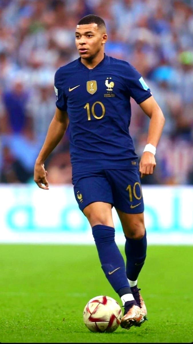 A soccer player in a blue France national team uniform with the number 10 is dribbling a ball on the field during a match, as seen on IPTV French, with a blurred crowd and stadium lights in the background.
